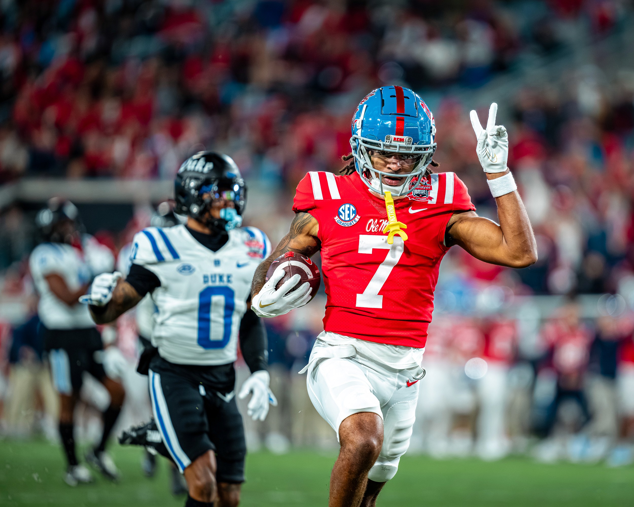 An Ole Miss receiver throws up a peace sign on the way to the end zone with a Duke defender trailing.
