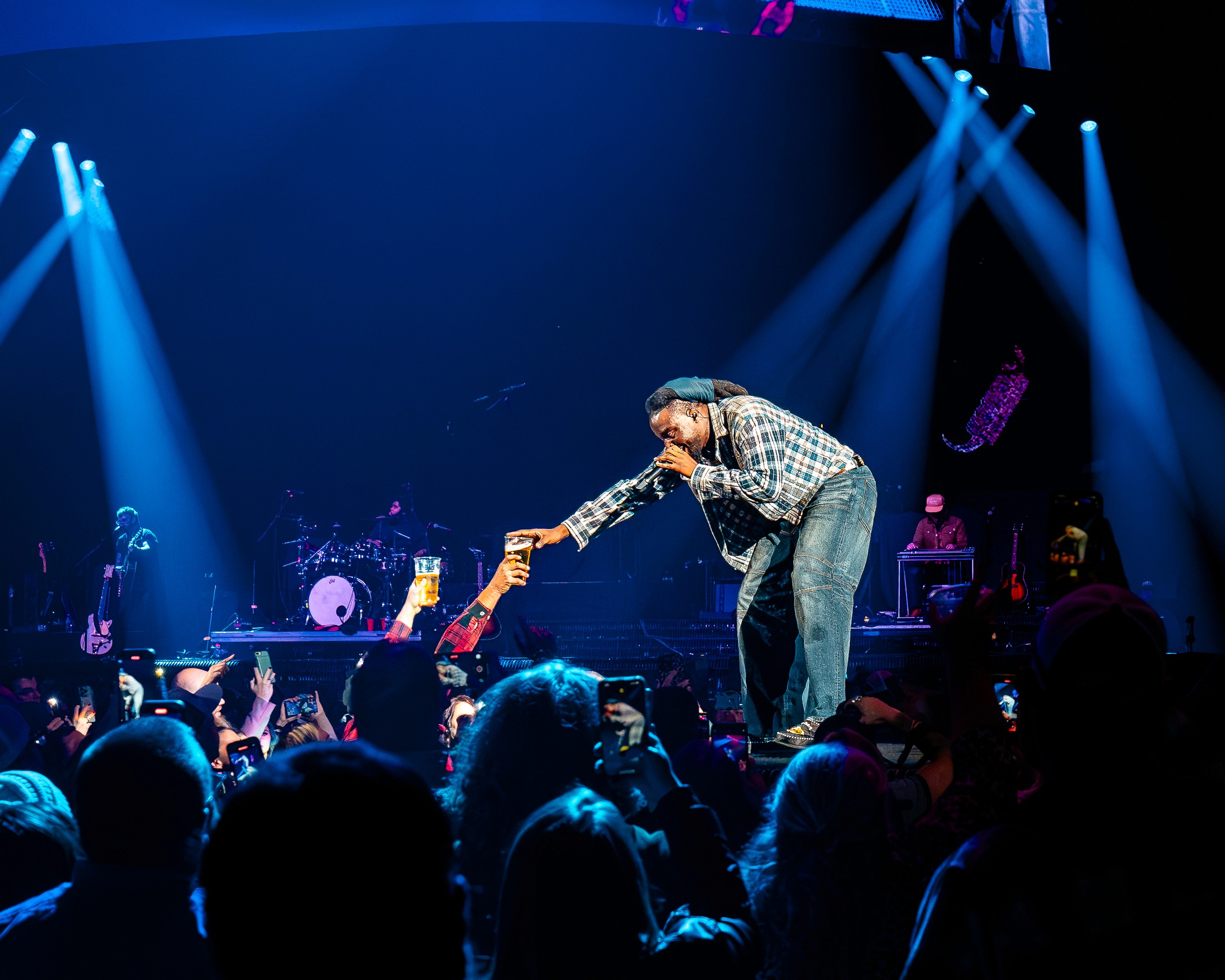 Shaboozey takes a beer from a fan at the edge of the stage.