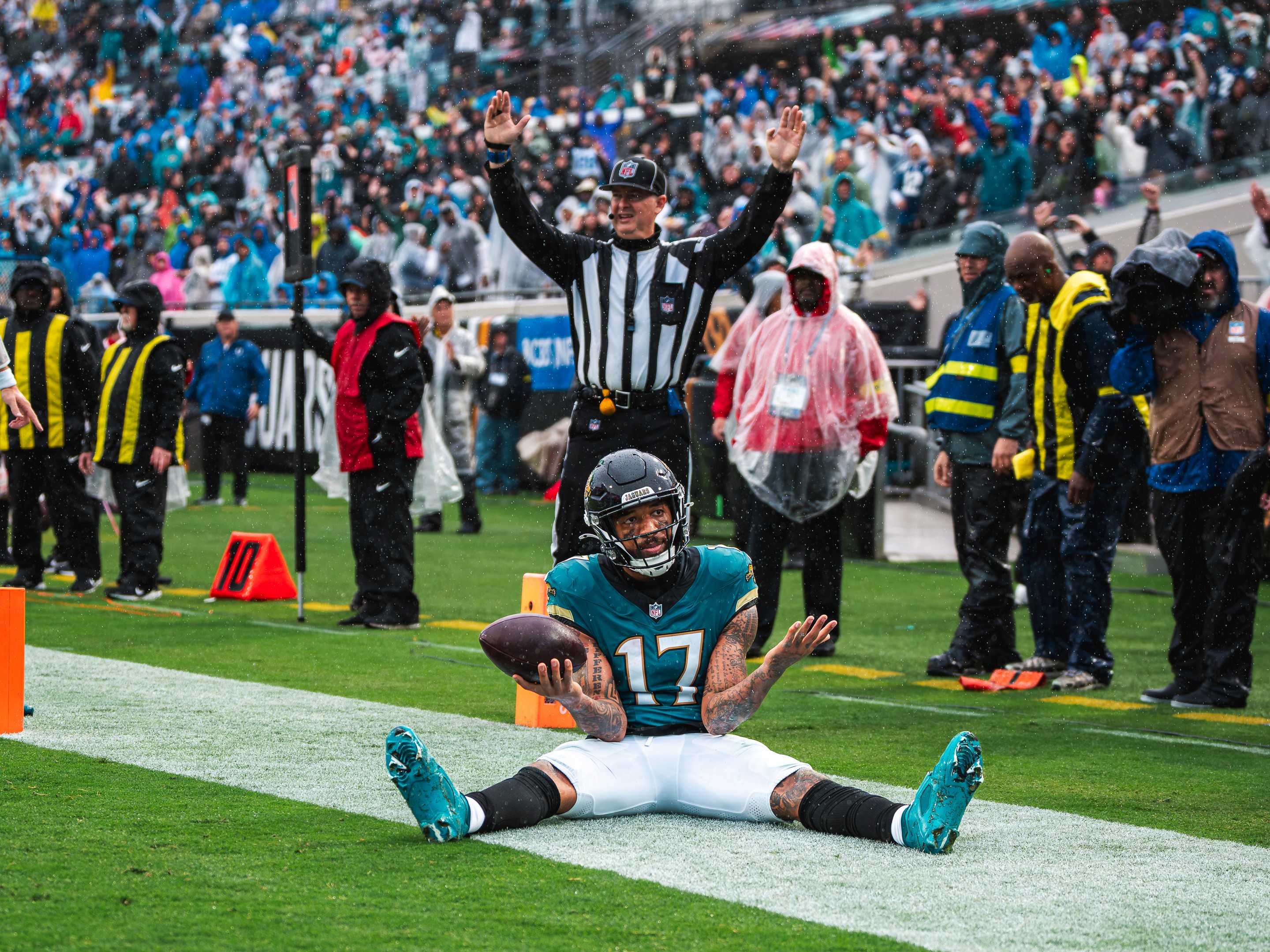A Jaguars receiver sits in the end zone with the ball as the back judge signals touchdown in the rain.