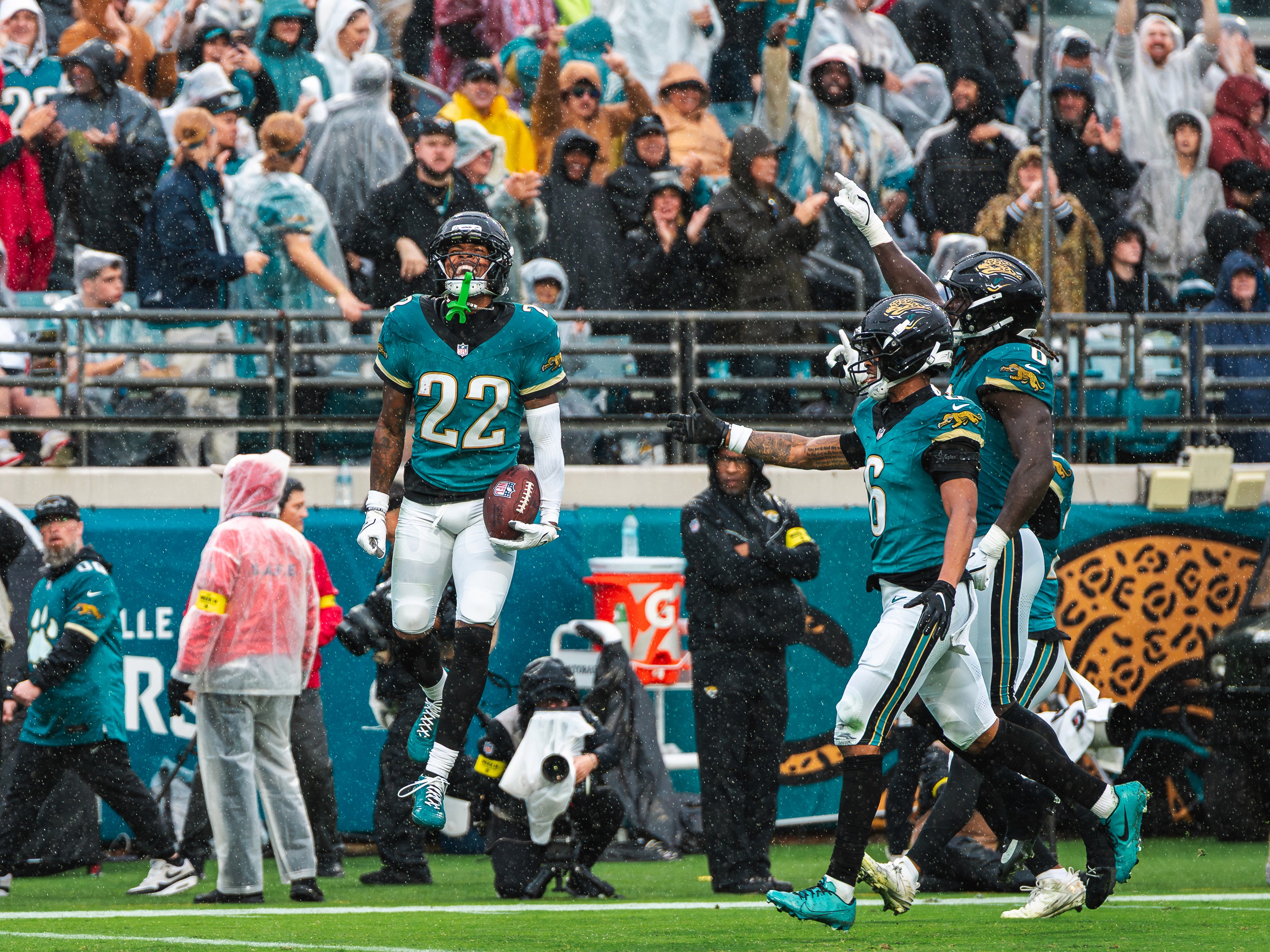 A Jaguars cornerback (22) hops with the ball after a turnover, teammates pointing to the stands.