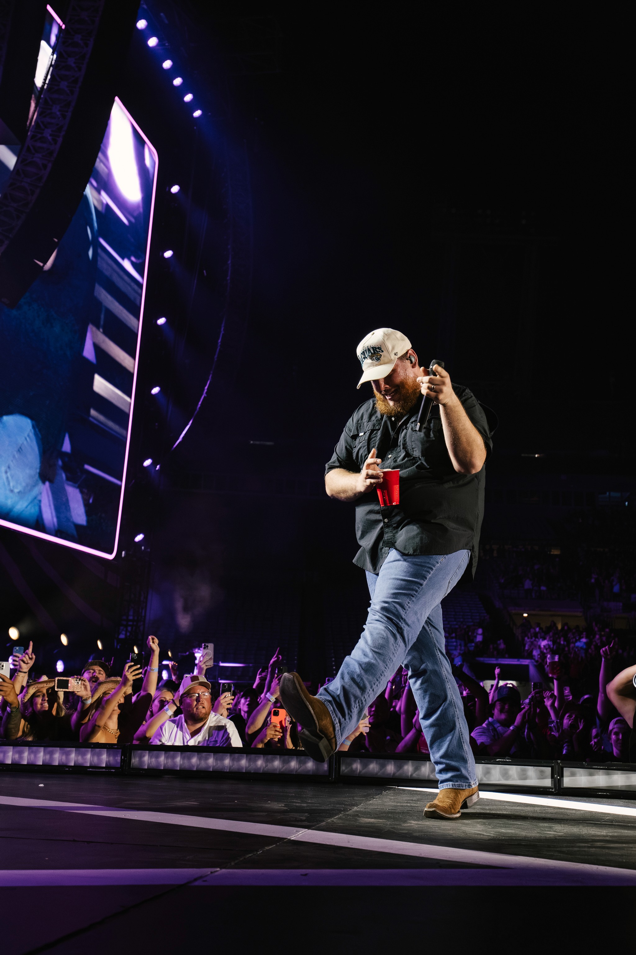 Luke Combs steps down the thrust toward the front rows, cup in hand.