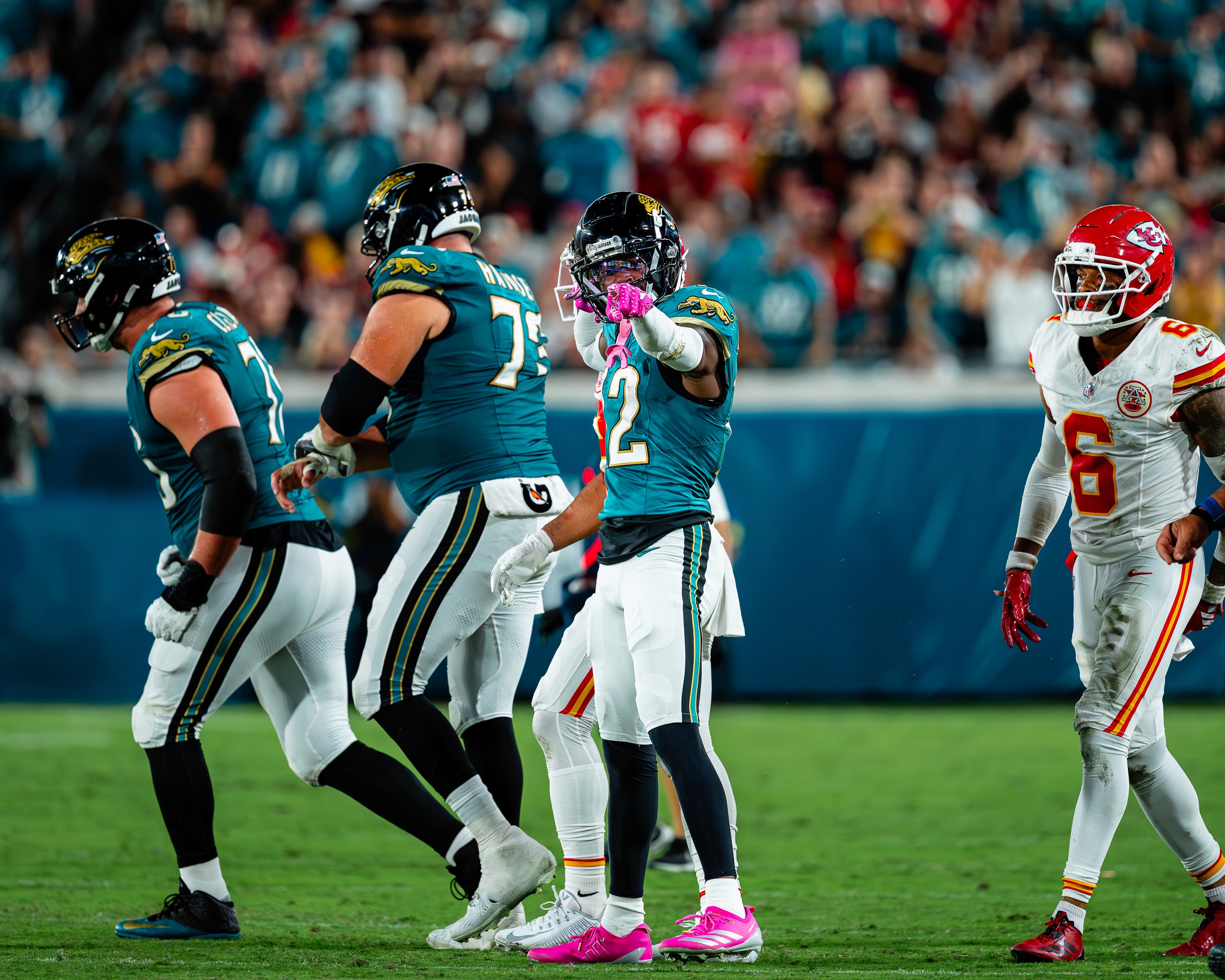 A Jaguars defender signals first down in pink Crucial Catch gloves as Chiefs safety Bryan Cook (6) walks off.