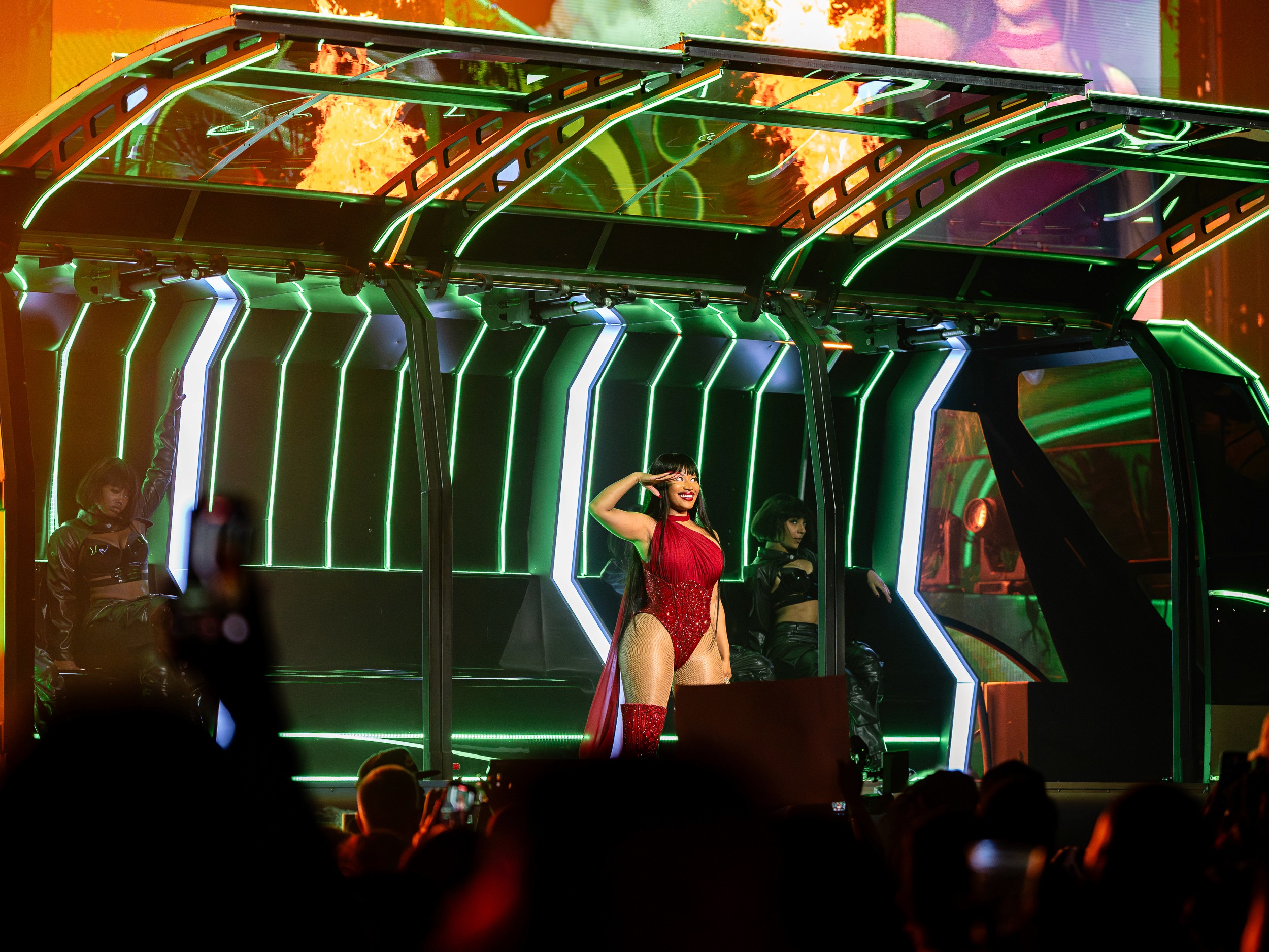 Nicki Minaj salutes from inside the neon stage set with dancers on either side.