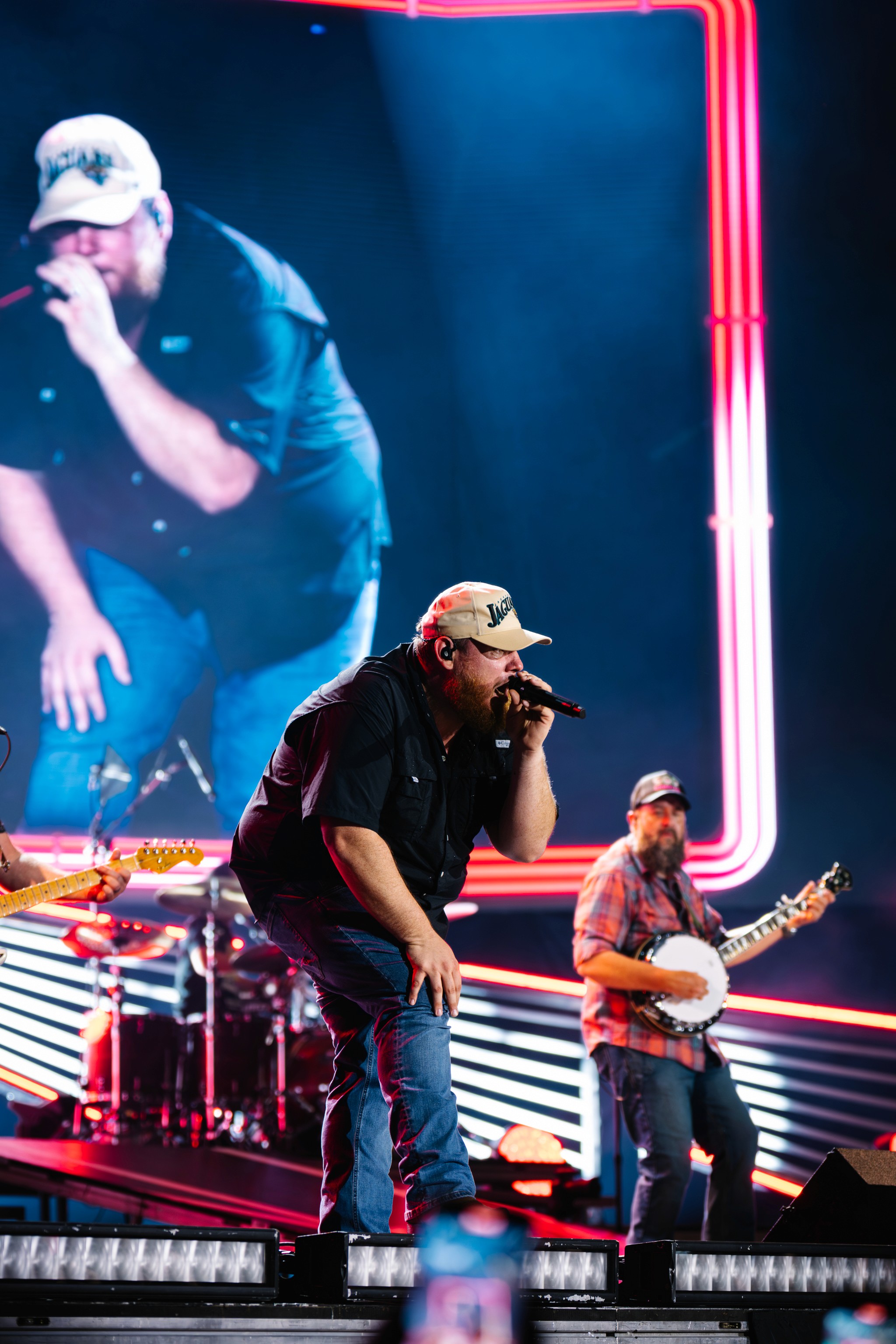 Luke Combs bent into the mic in front of the drum kit and the banjo, his image on the screen behind.