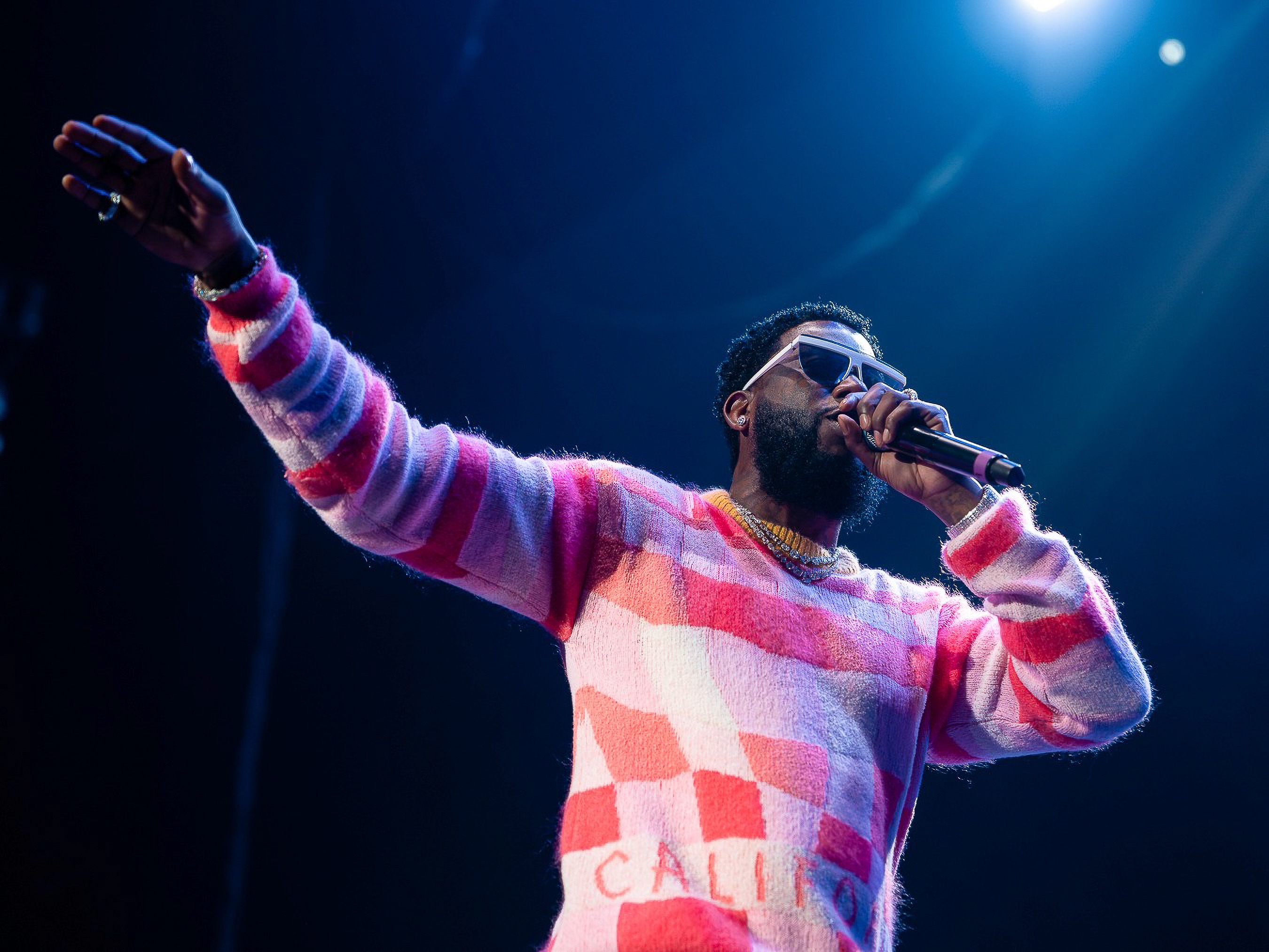 Gucci Mane, one hand up to the crowd, under a blue backlight at VyStar Veterans Memorial Arena in Jacksonville.