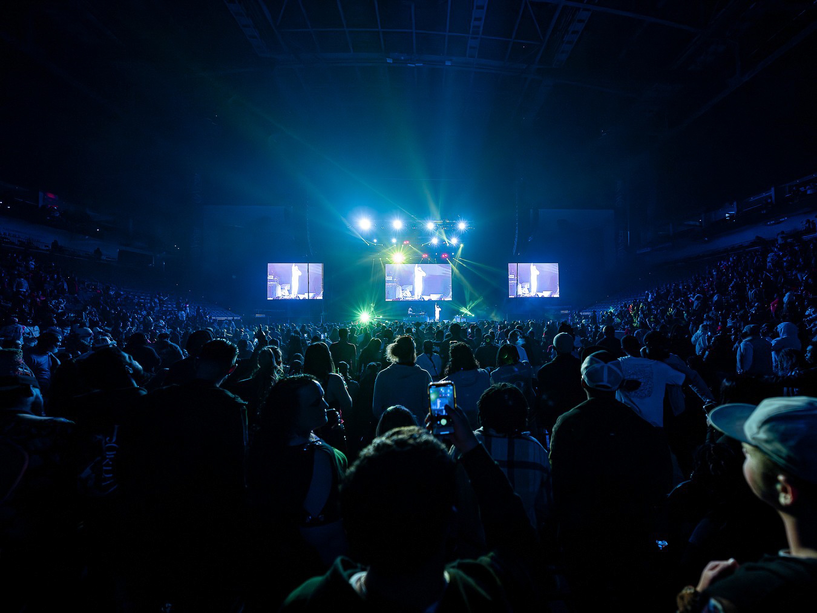 The floor of VyStar Veterans Memorial Arena from the back of the crowd, three screens over the stage.