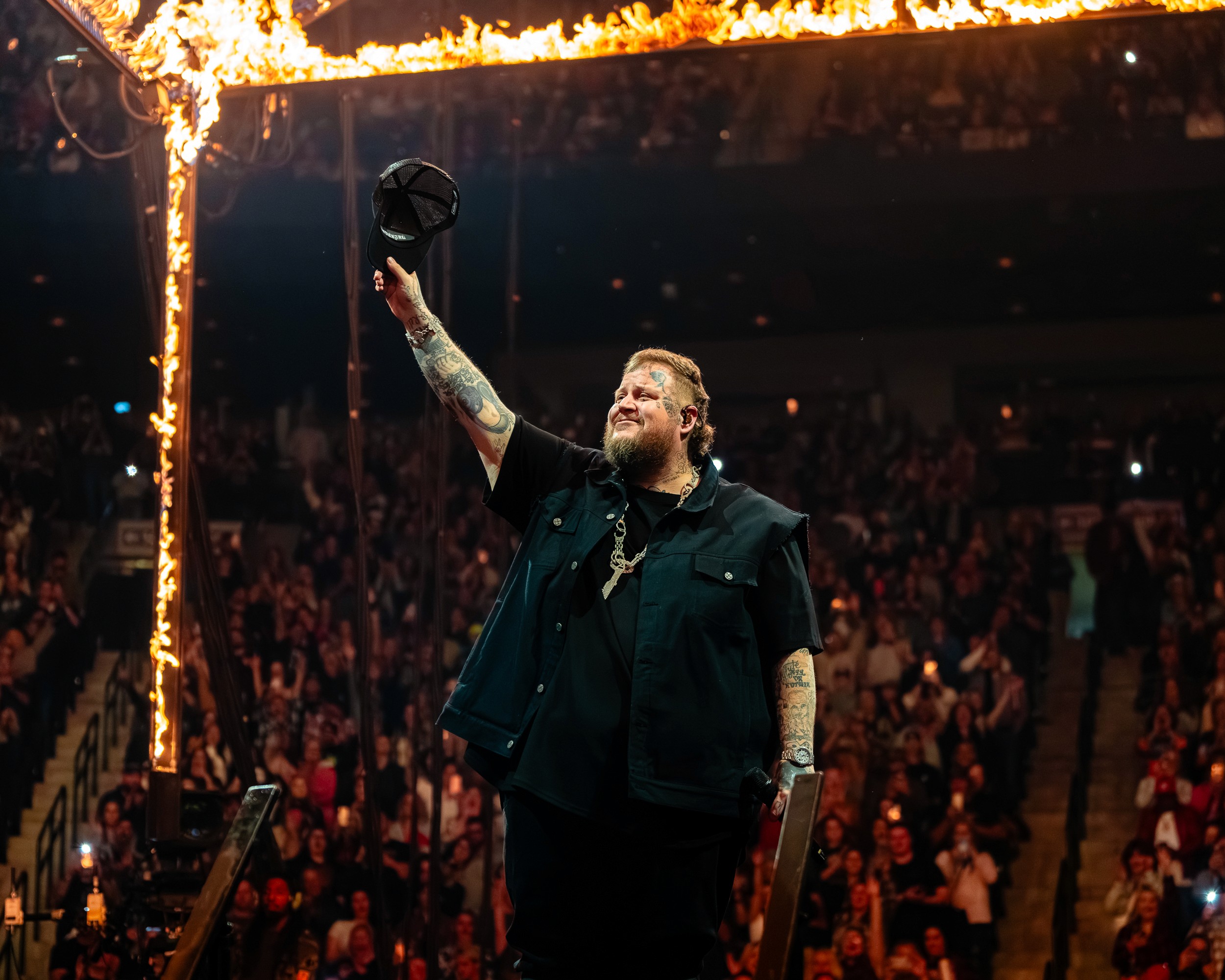 Cap raised to the crowd beneath the flaming frame.