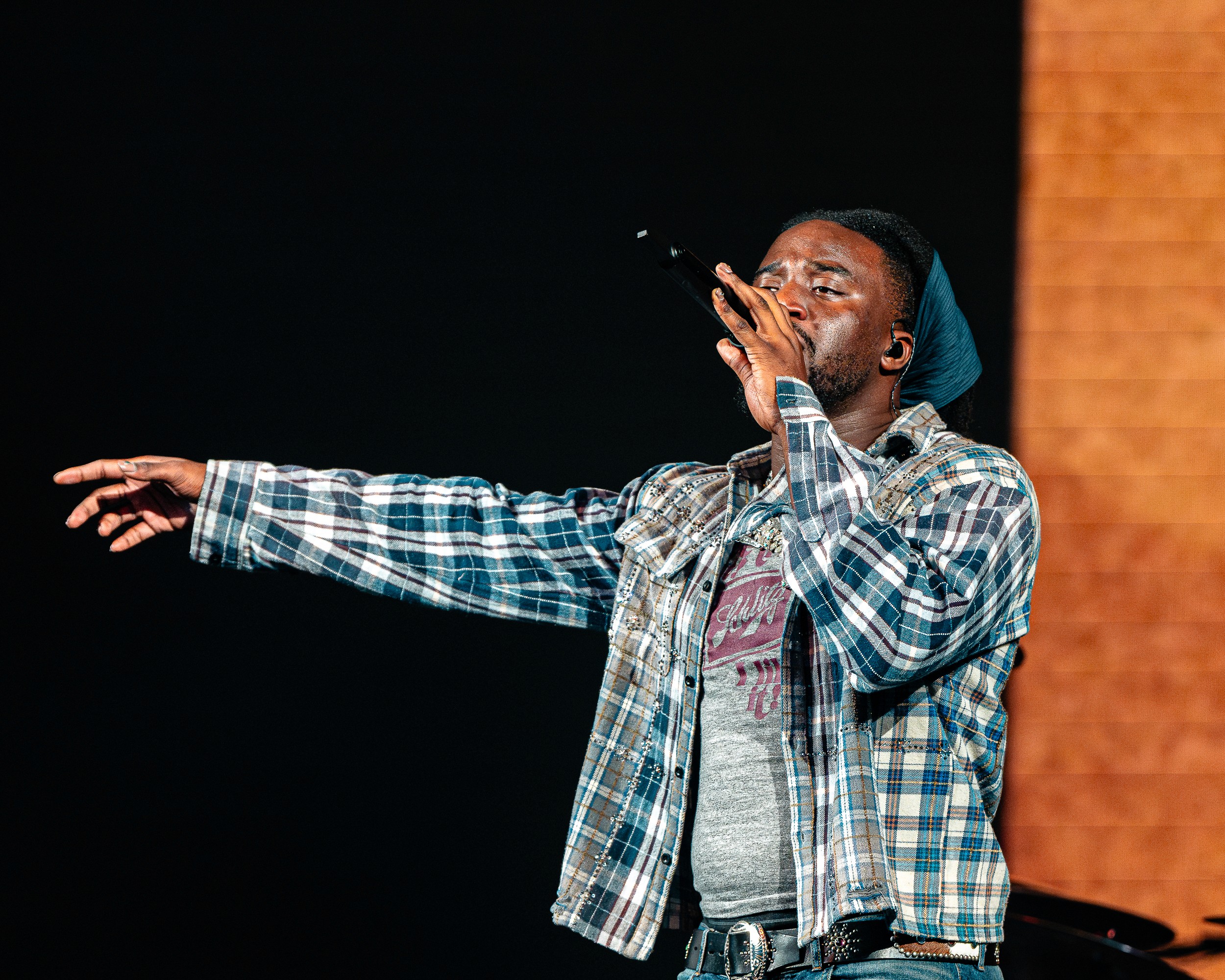 Shaboozey mid-verse in plaid, one arm pointed to the crowd.