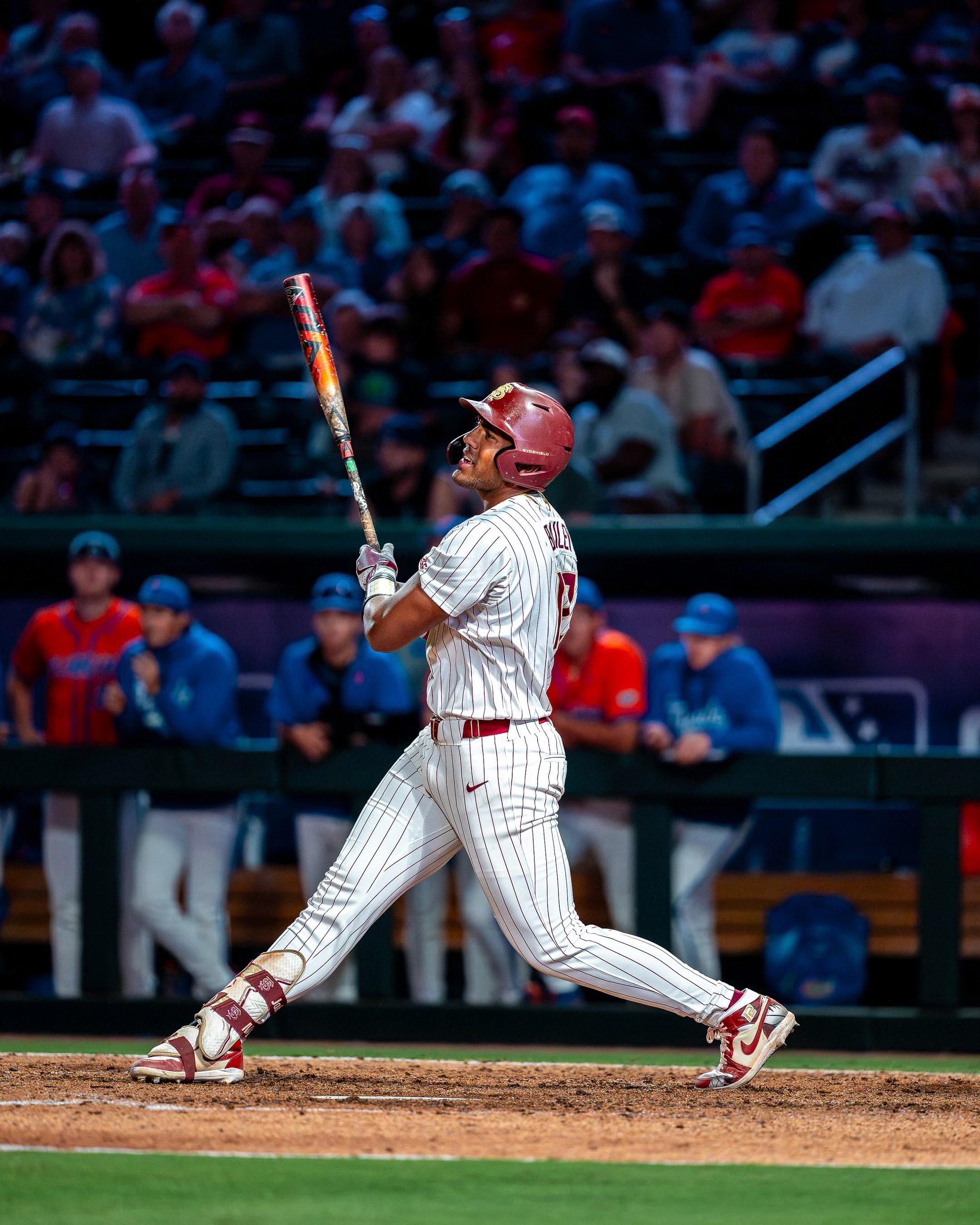 A Florida State hitter follows his drive from the box with the Florida dugout behind him.