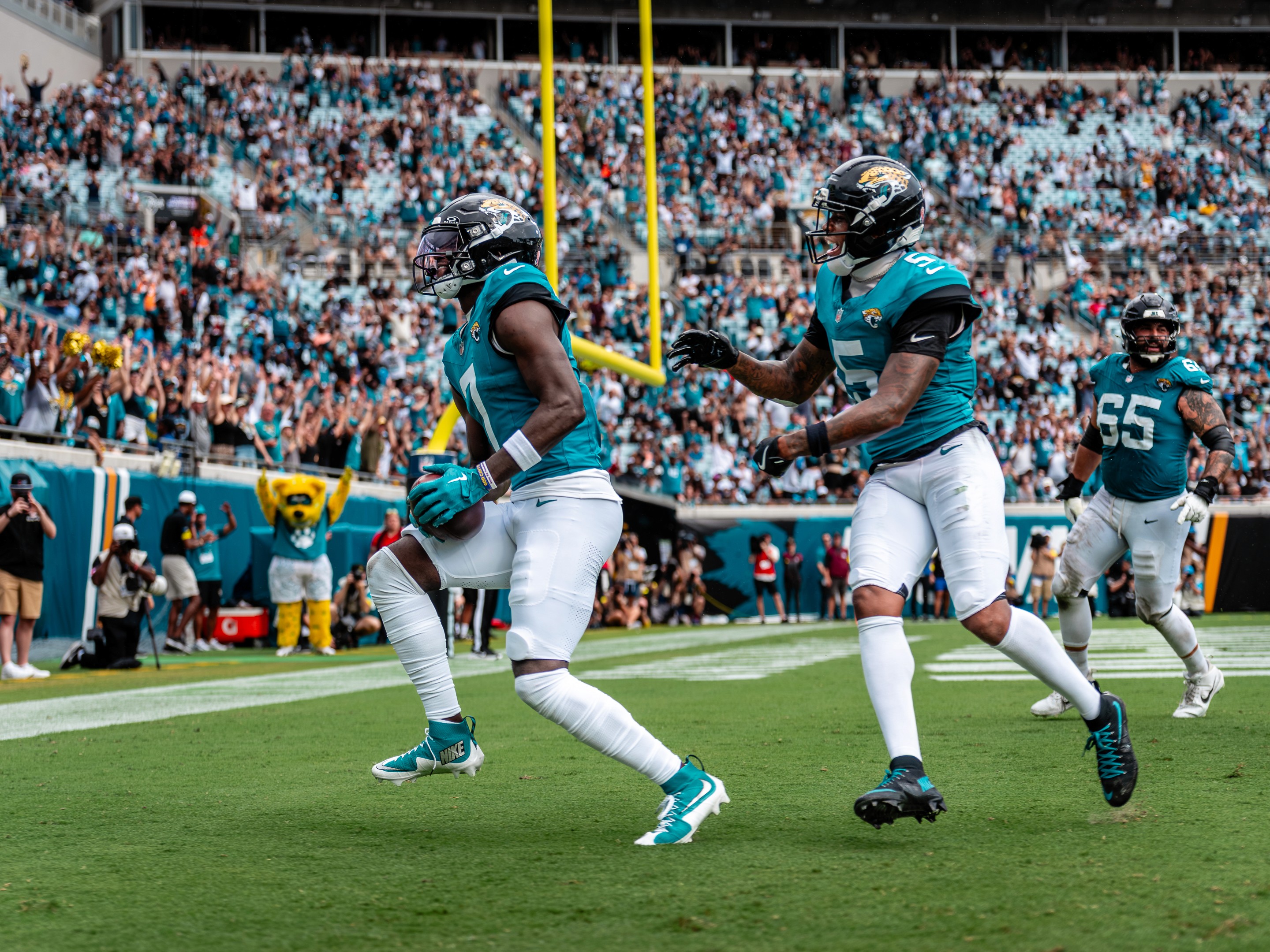 Two Jaguars celebrate a touchdown under the uprights, Jaxson de Ville watching from the sideline.