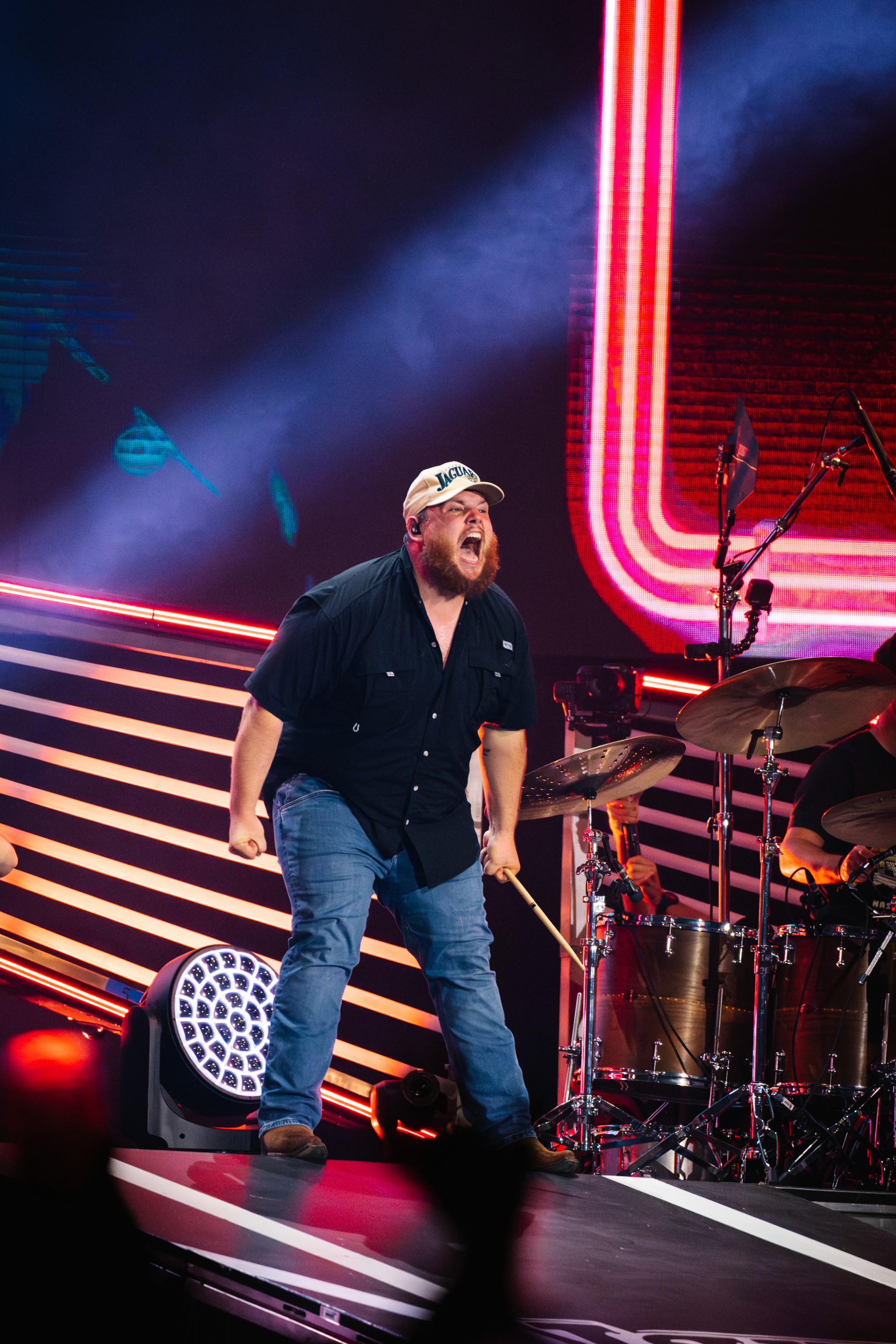 Luke Combs in a Jaguars cap shouting to the crowd in front of the drum riser at EverBank Stadium.