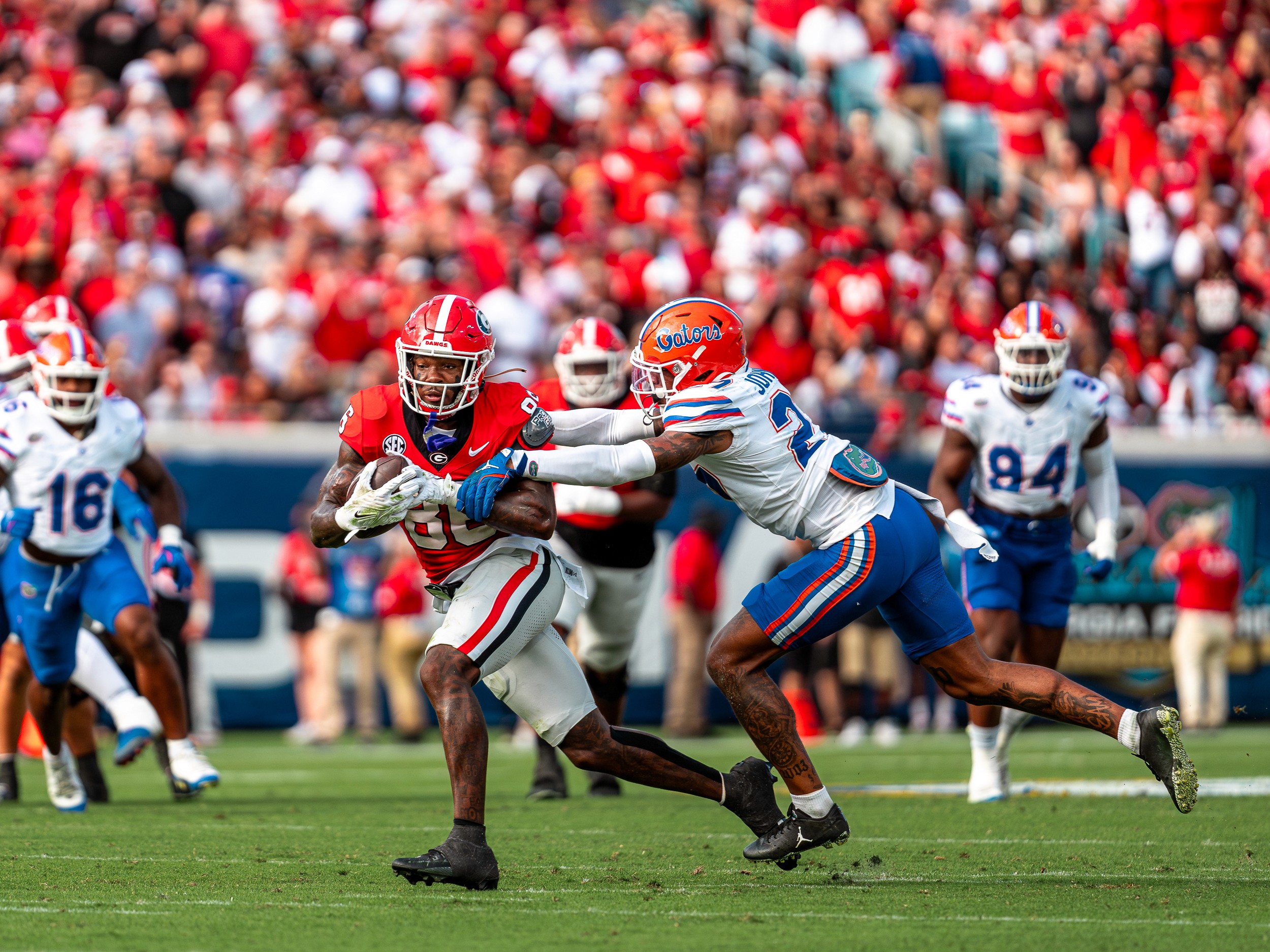 A Georgia ball carrier is wrapped up by a Florida defender in the open field, the red-and-blue crowd behind.