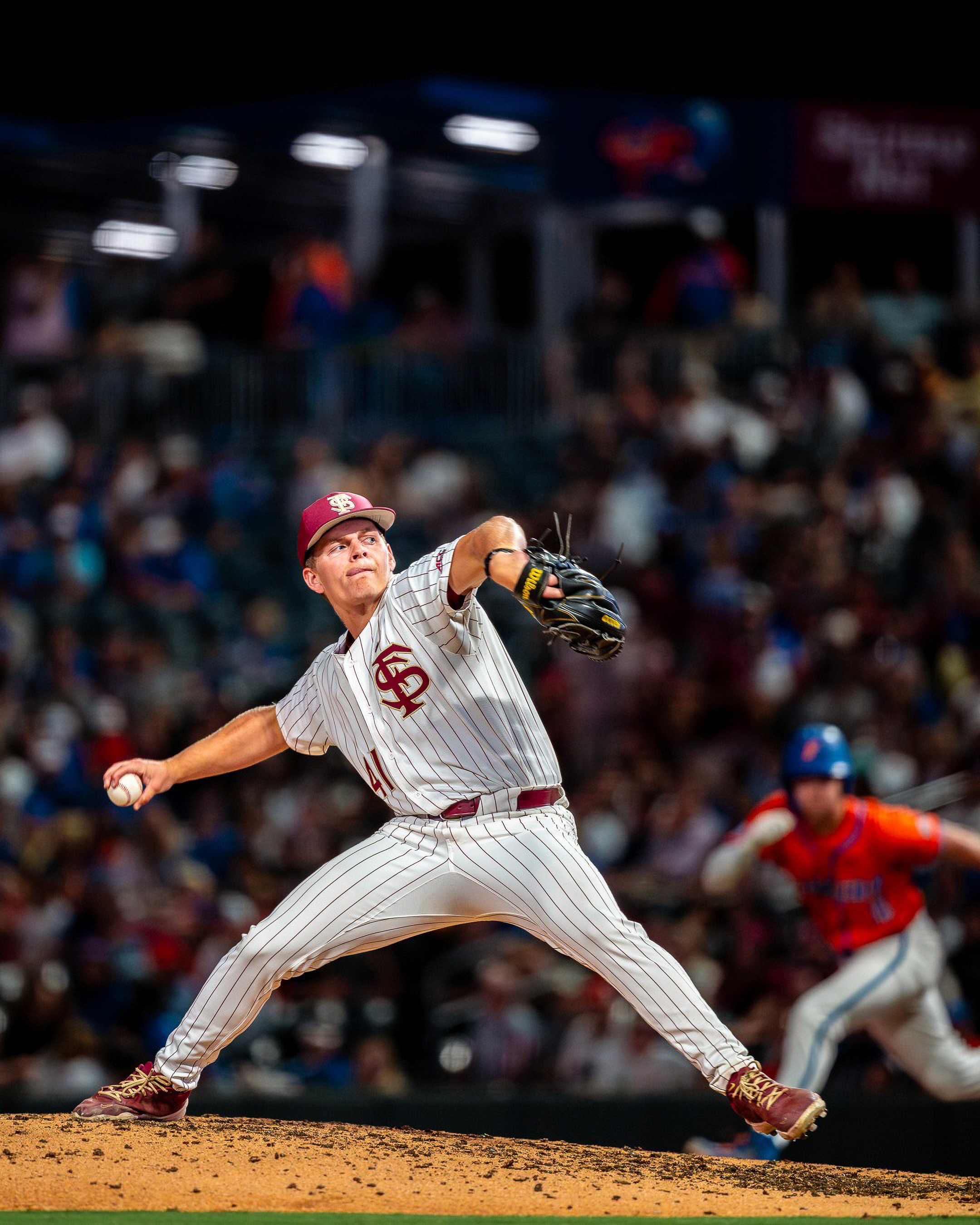 A Florida State pitcher drives off the mound as a Florida runner takes his lead in the background.