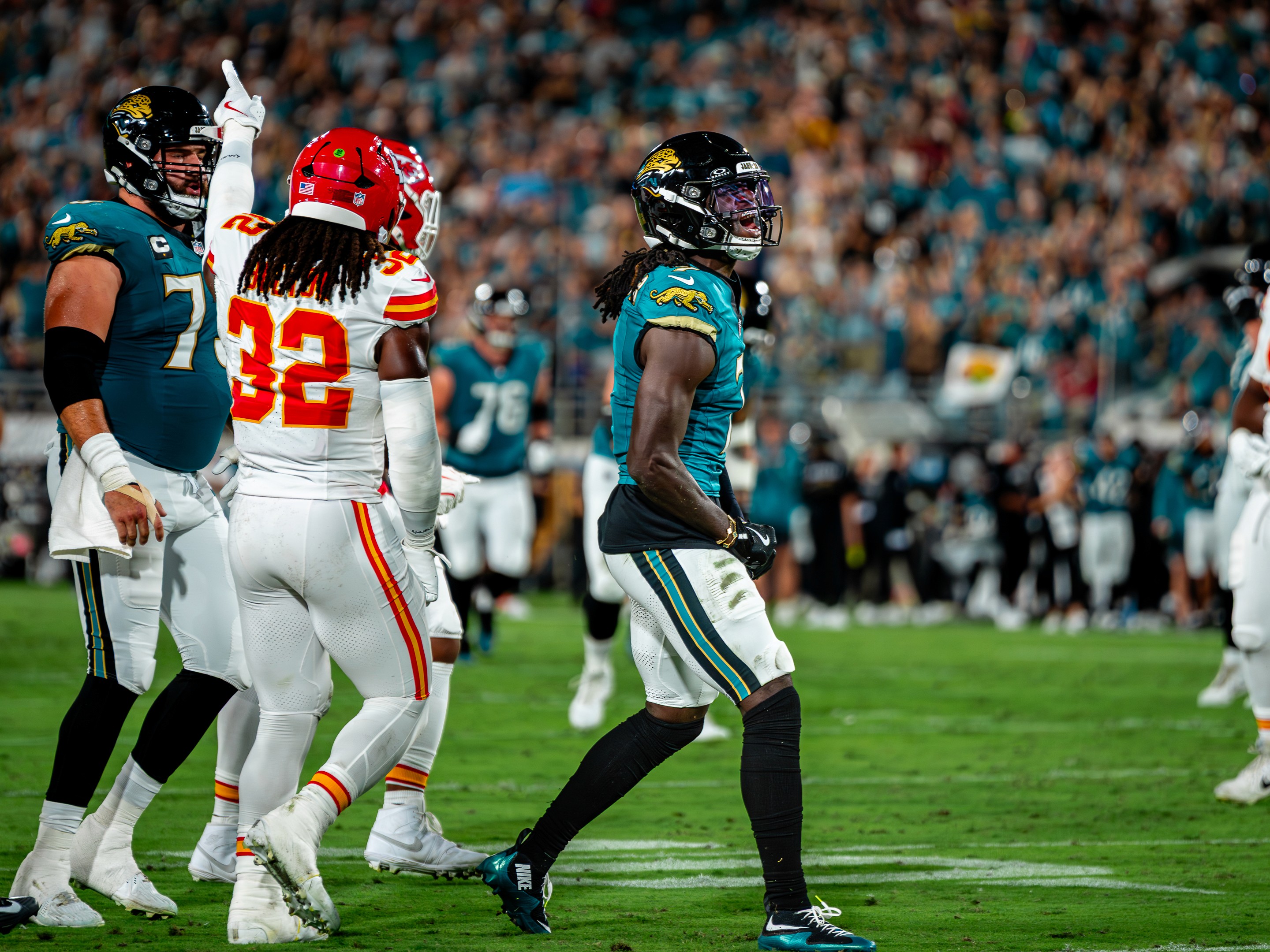 Between plays: a Jaguar looks back to the huddle as Chiefs linebacker Nick Bolton (32) points downfield.