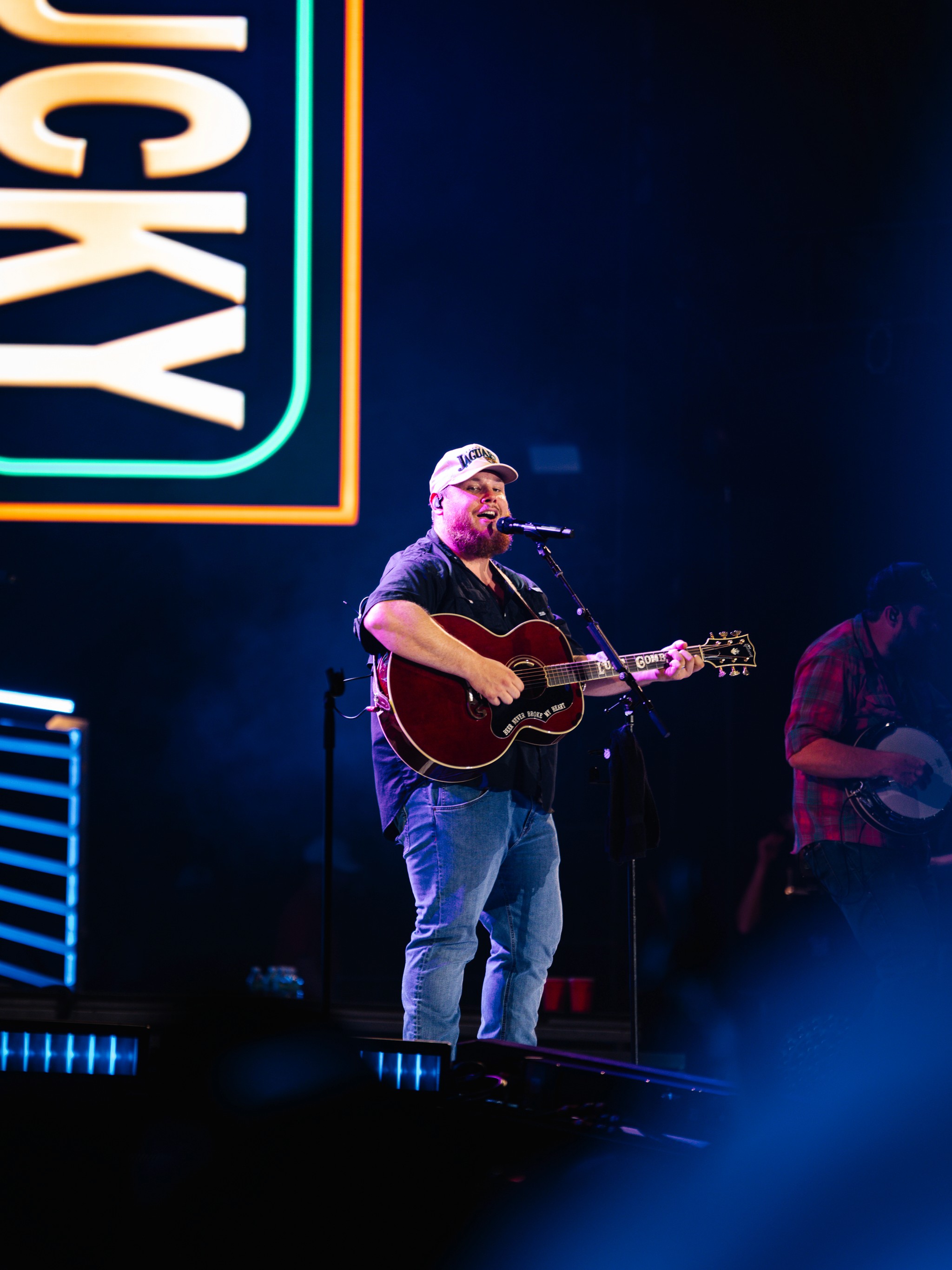Luke Combs on acoustic guitar with the banjo player behind him, LUCKY on the screen.