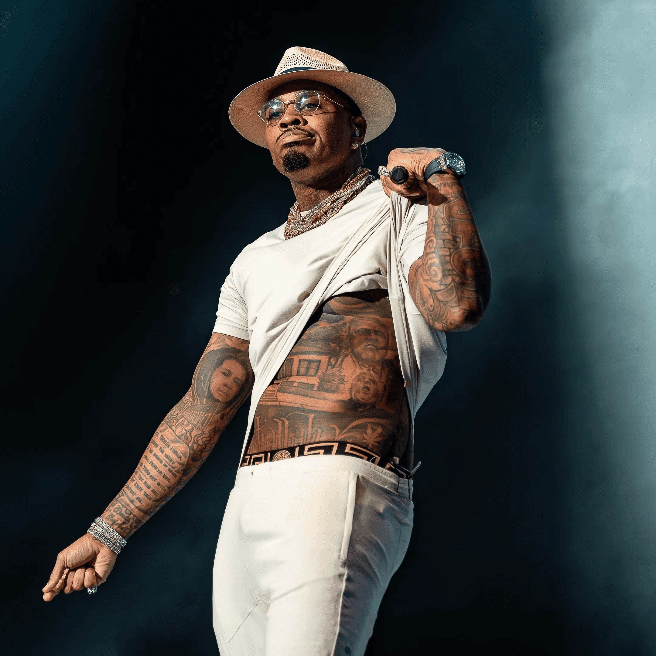 A supporting act pulls up his shirt to show the tattoos under a blue wash.